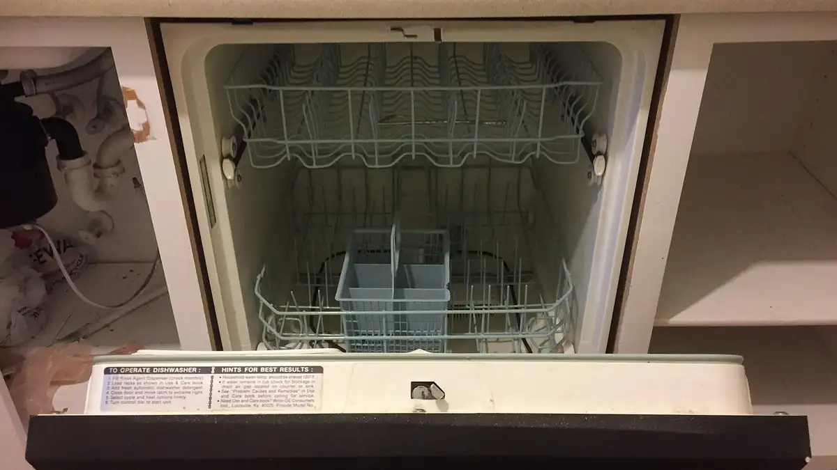A built-in dishwasher with its door open under a kitchen worktop