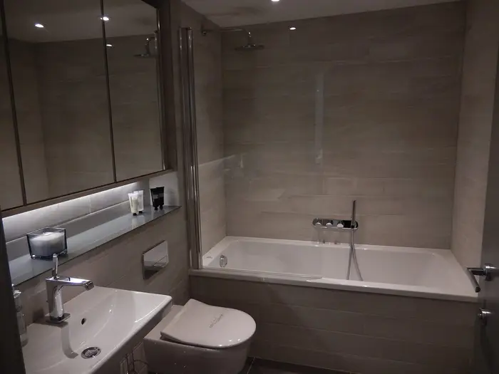 A modern grey-tiled bathroom with a bath, basin and wall-hung toilet