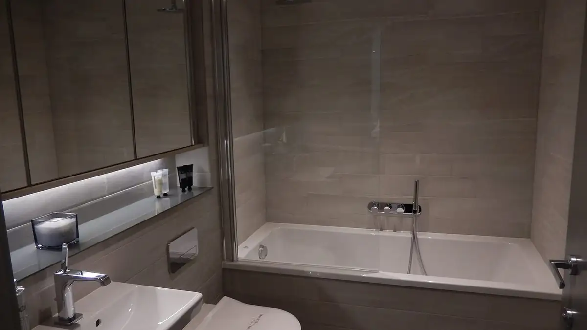 A modern grey-tiled bathroom with a bath, basin and wall-hung toilet