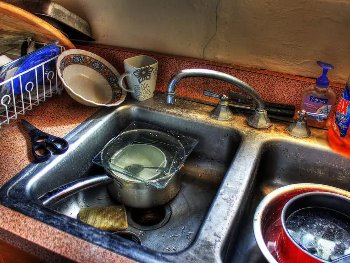 A kitchen sink with standing water, pans and dishes
