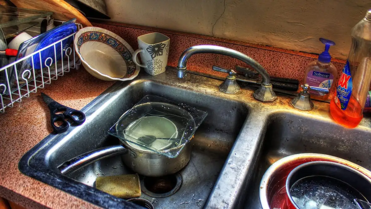 A kitchen sink with standing water, pans and dishes