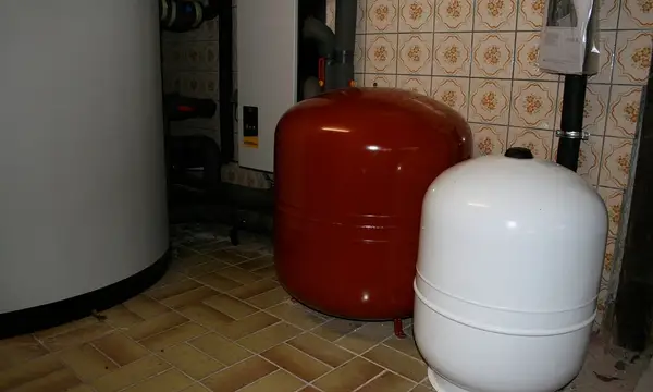 Red and white expansion vessels standing on a tiled floor beside a hot water tank