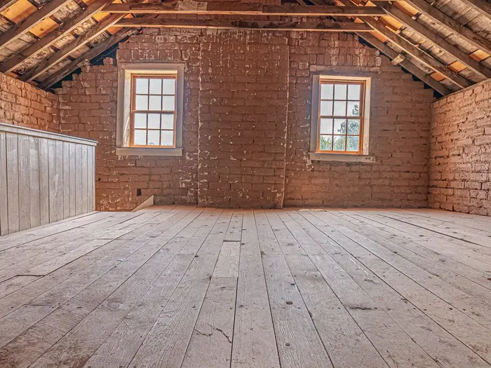 A boarded loft space with brick walls and two small windows