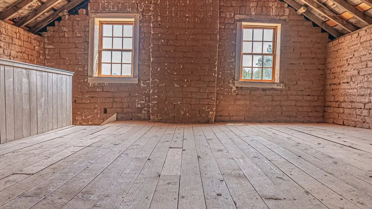 A boarded loft space with brick walls and two small windows