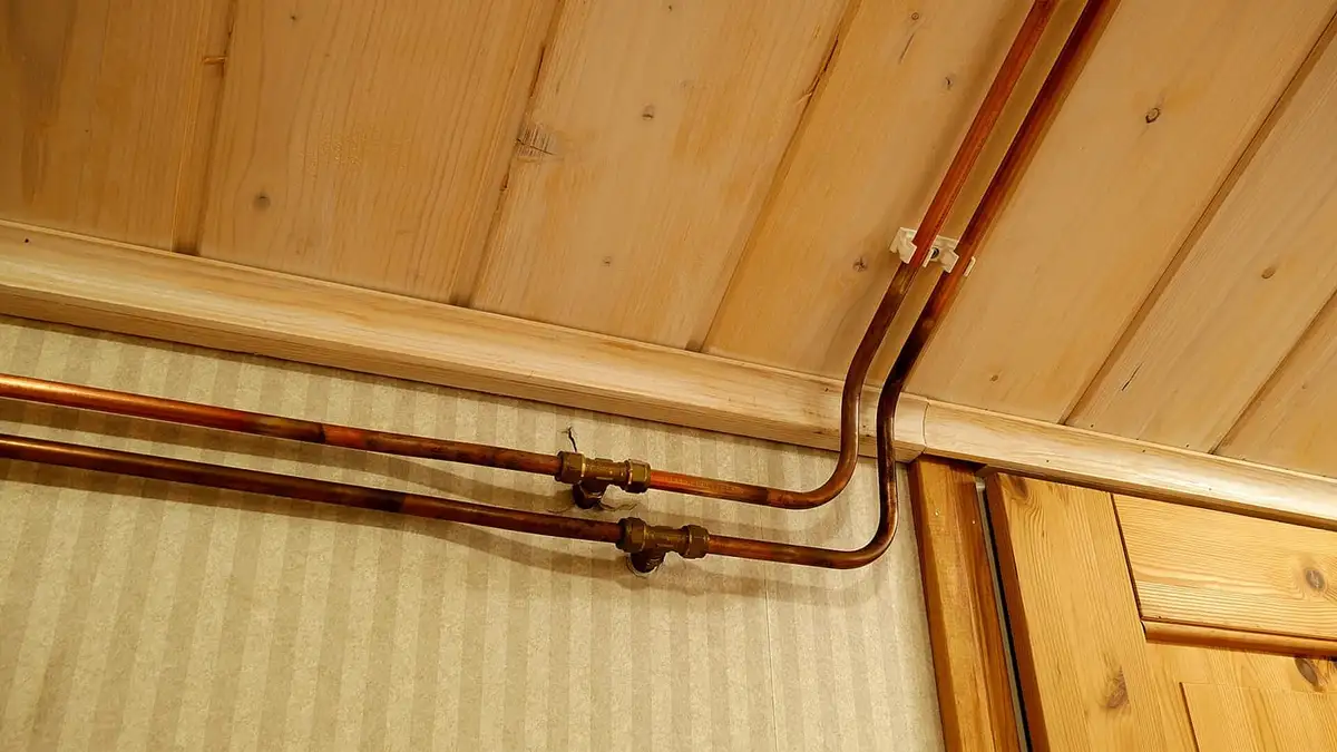 Copper water pipes running along a wall above the skirting