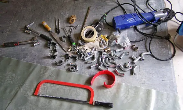 Plumbing tools and fittings laid out on a dust sheet, with a hacksaw and pipe bender