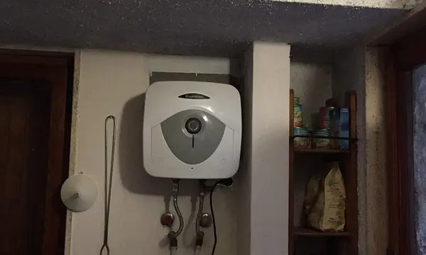 A small electric water heater on a wall with its water connections below
