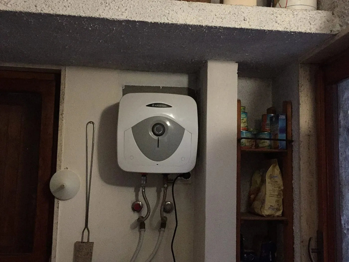 A small electric water heater on a wall with its water connections below