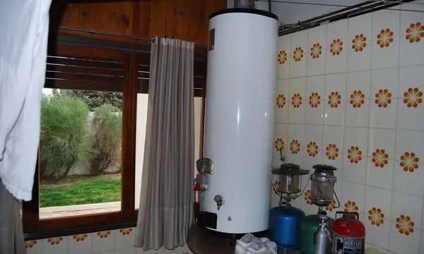 A tall white hot water storage tank standing in a tiled room