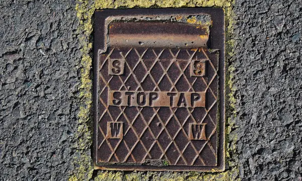 A cast iron stop tap cover set into a pavement