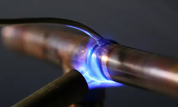 A blue torch flame soldering a joint on copper pipe