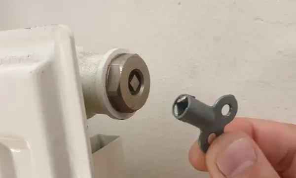 A radiator bleed key held next to the bleed valve of a white radiator