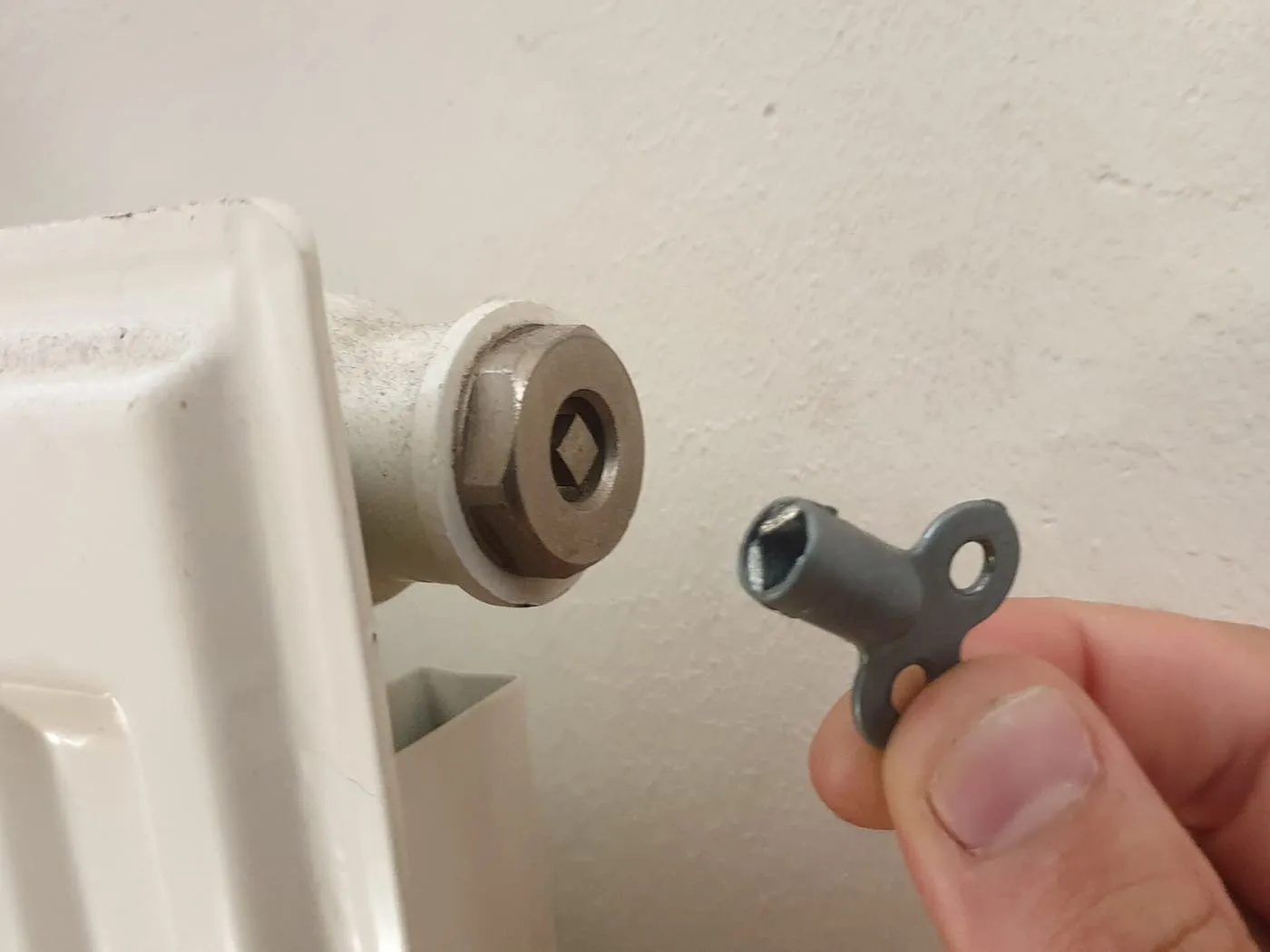 A radiator bleed key held next to the bleed valve of a white radiator