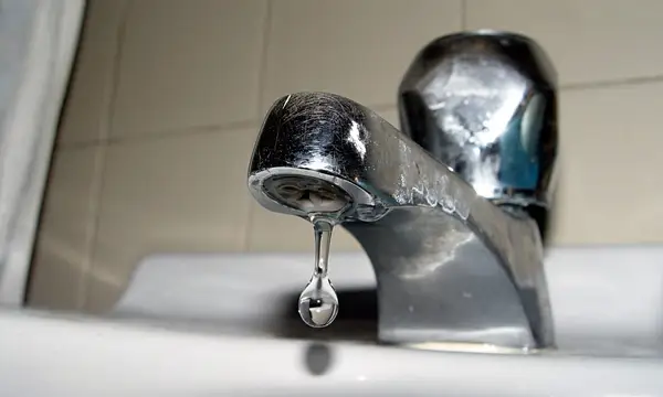 A drop of water falling from a chrome basin tap