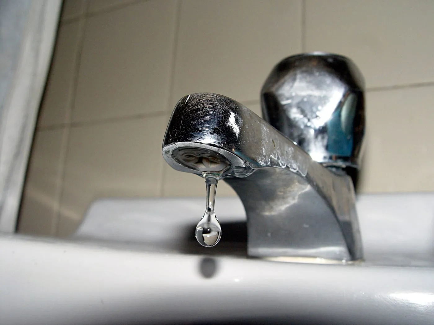 A drop of water falling from a chrome basin tap