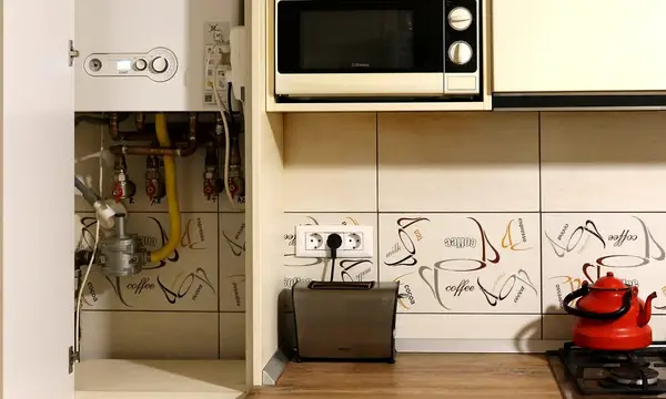 A wall-mounted boiler fitted in a kitchen cupboard beside a microwave