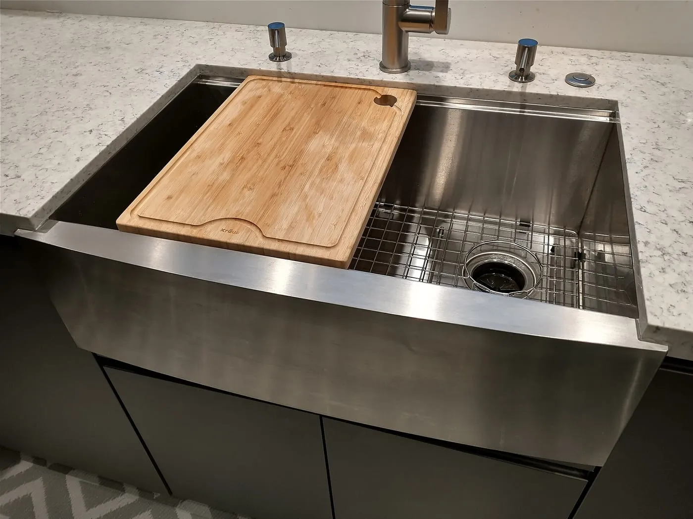 A stainless steel farmhouse kitchen sink with a wooden chopping board and mixer tap