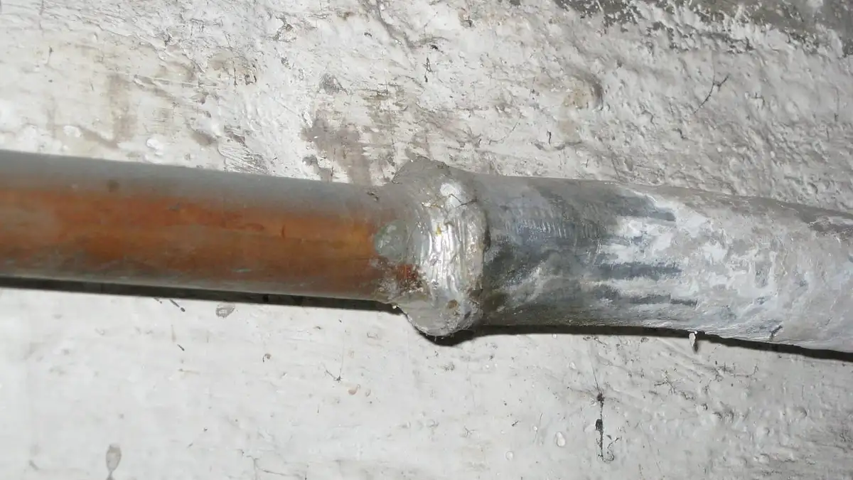 An old lead water pipe joined to copper pipe on a whitewashed wall