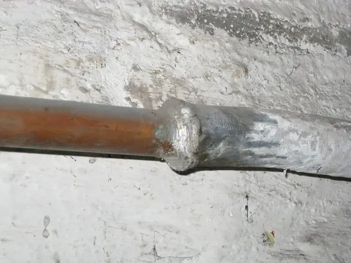 An old lead water pipe joined to copper pipe on a whitewashed wall