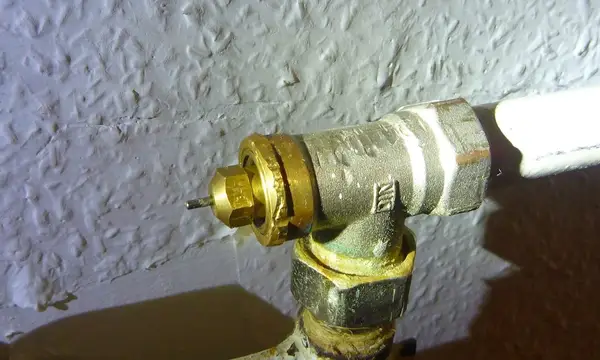 A brass radiator valve on a heating pipe against a textured wall