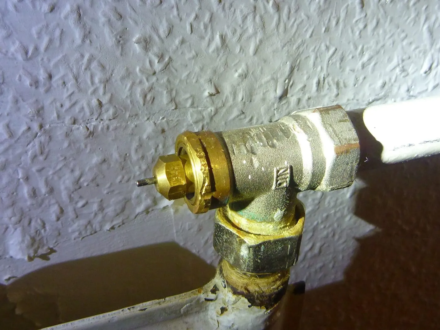 A brass radiator valve on a heating pipe against a textured wall