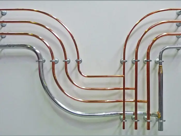 Bent copper and steel pipes run in parallel on a white wall
