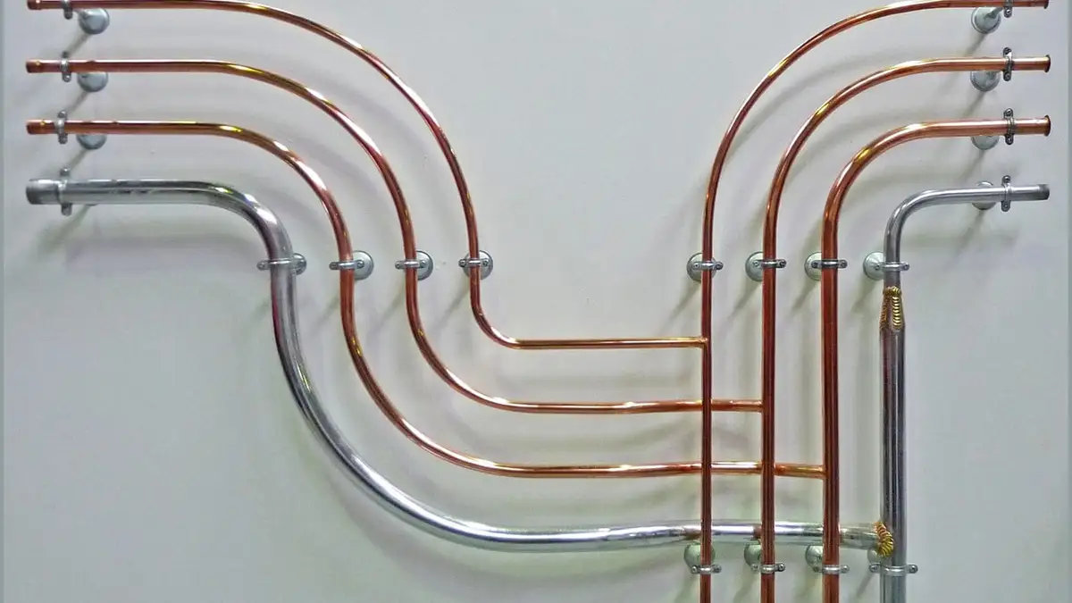 Bent copper and steel pipes run in parallel on a white wall