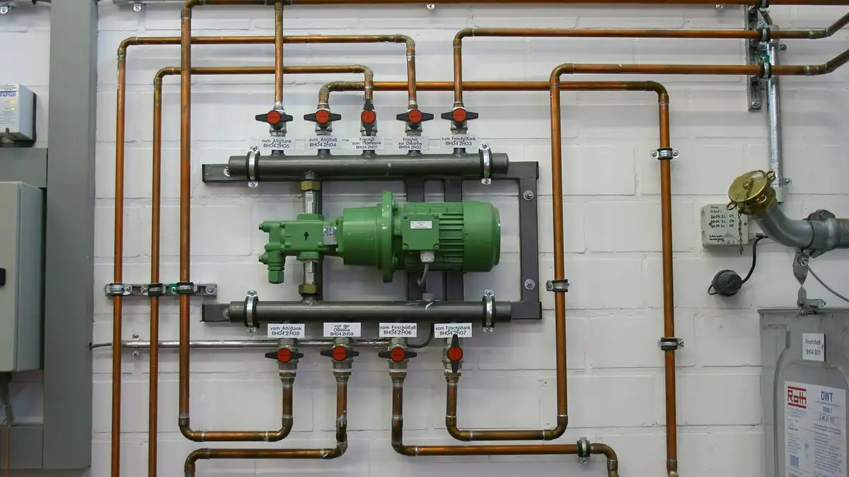 A heating manifold and circulating pump on copper pipework against a white wall