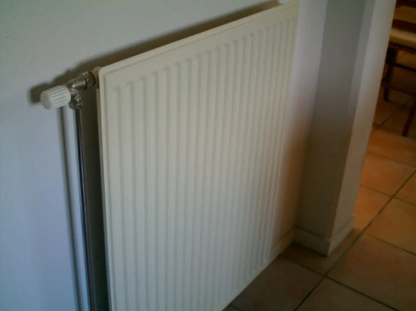 A white panel radiator on a wall above a tiled floor