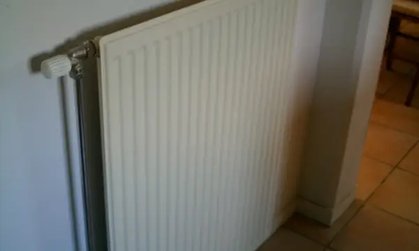 A white panel radiator on a wall above a tiled floor