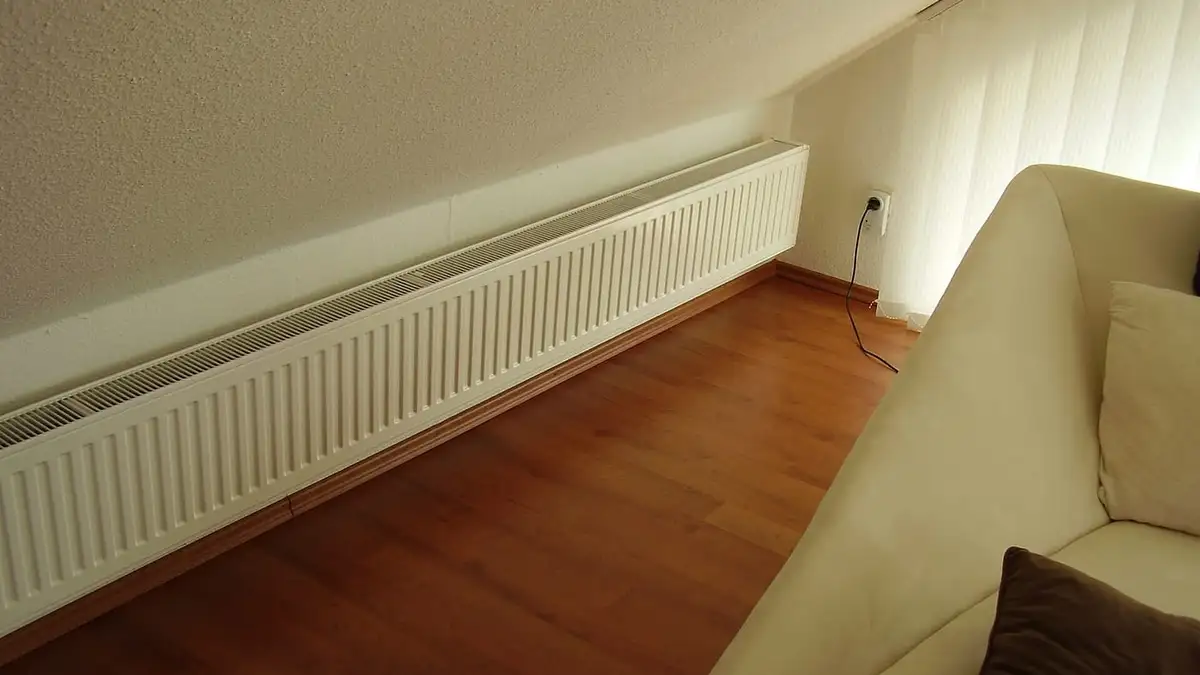 A long white panel radiator under a sloping ceiling in a room with a wooden floor