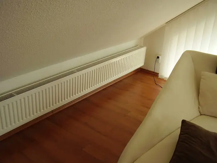 A long white panel radiator under a sloping ceiling in a room with a wooden floor