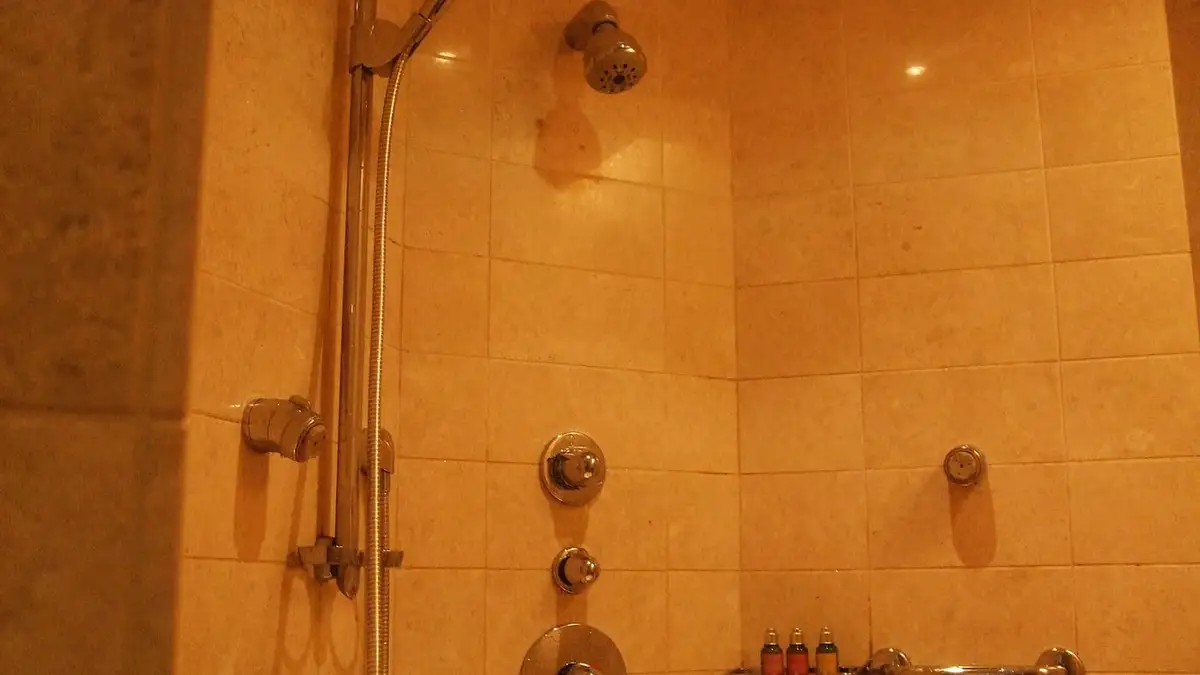 A tiled shower with a riser rail, body jets and thermostatic controls
