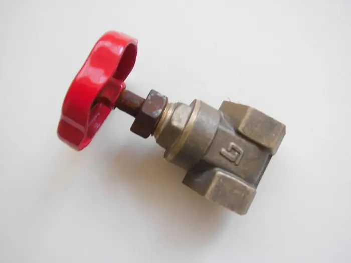 A brass stop valve with a red wheel handle