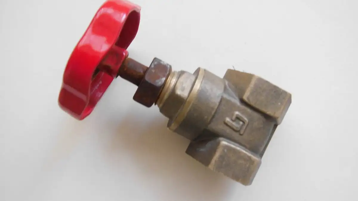 A brass stop valve with a red wheel handle