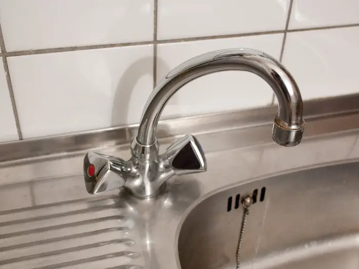 A chrome swan-neck mixer tap over a stainless steel kitchen sink