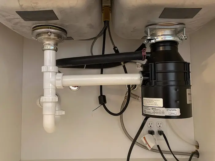 A food waste disposal unit fitted under a kitchen sink with its waste pipework