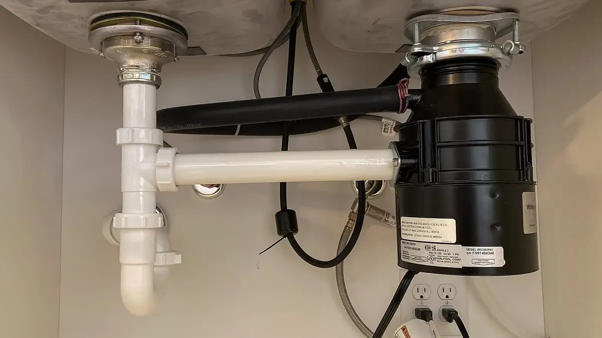 A food waste disposal unit fitted under a kitchen sink with its waste pipework