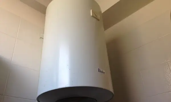 A white electric storage water heater mounted on a tiled wall