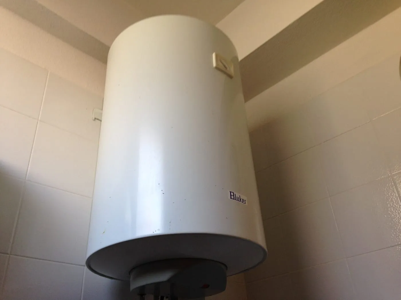 A white electric storage water heater mounted on a tiled wall