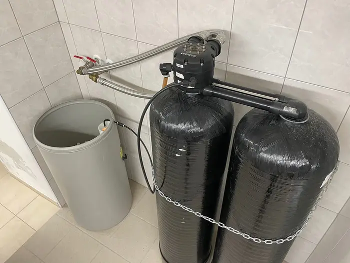A twin-cylinder water softener with its salt tank in a tiled room