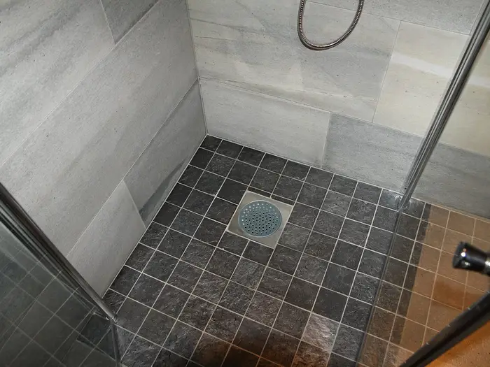 A level-access shower floor with dark tiles falling to a central drain