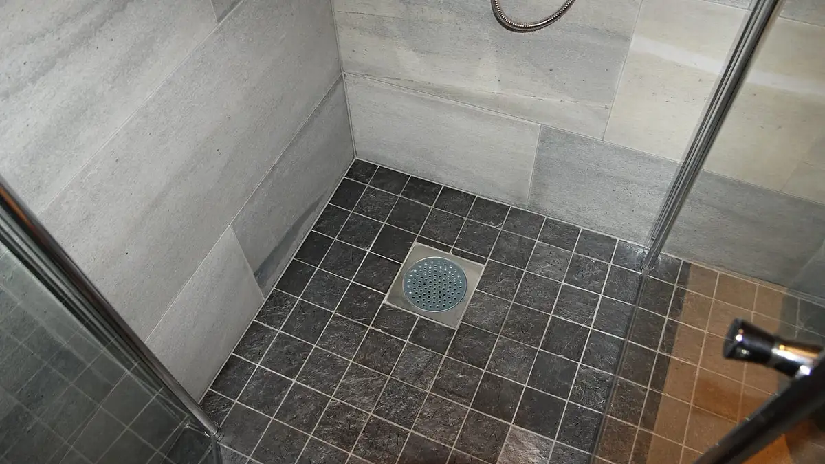 A level-access shower floor with dark tiles falling to a central drain