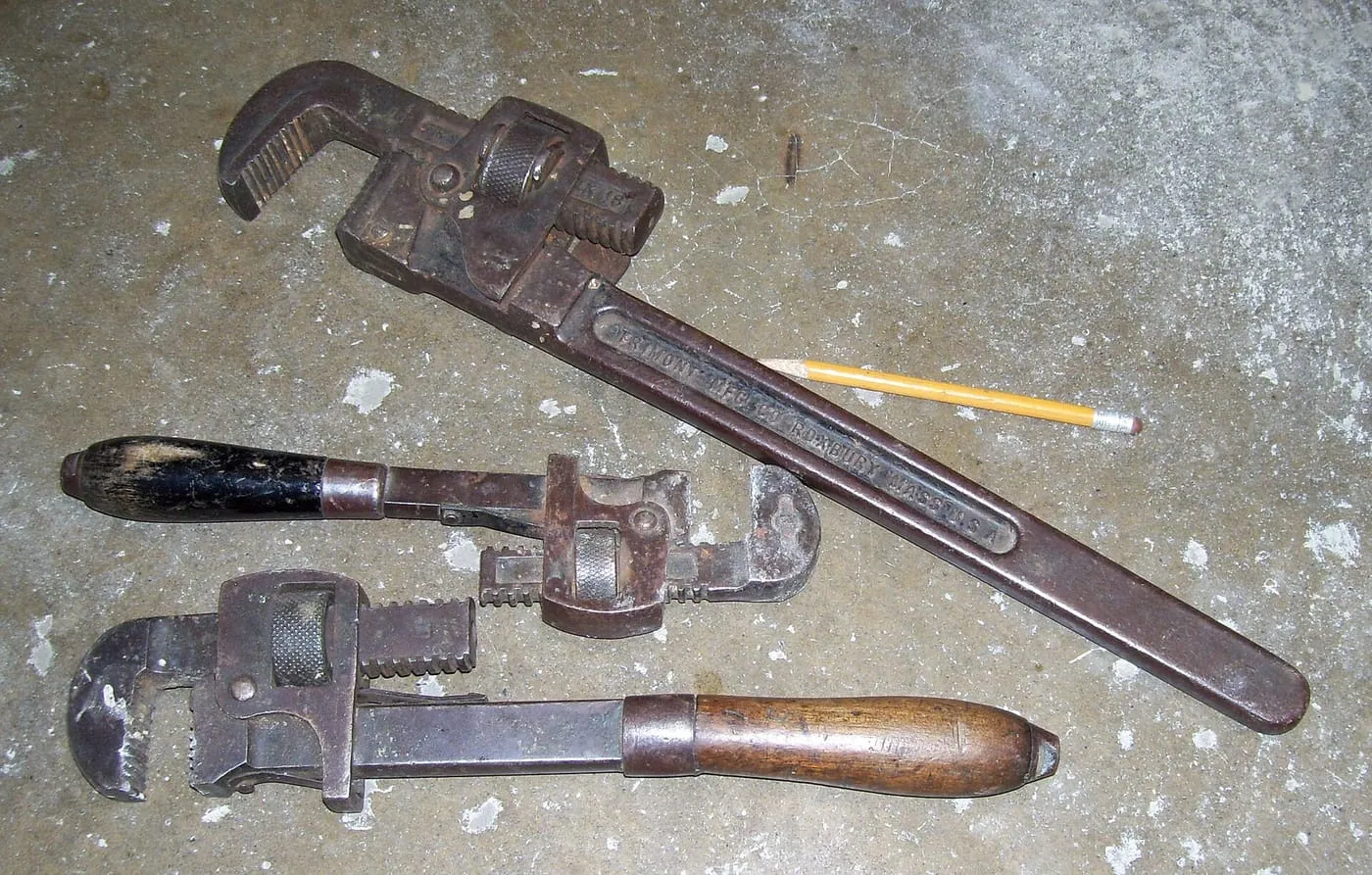 Three pipe wrenches lying on a workshop floor