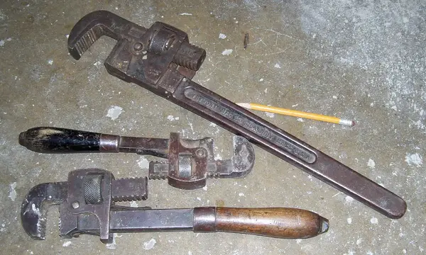 Three pipe wrenches lying on a workshop floor